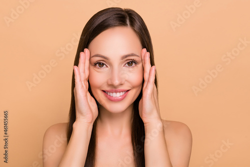 Photo of shiny charming mature woman naked shoulders doing face massage fingers temples smiling isolated beige color background