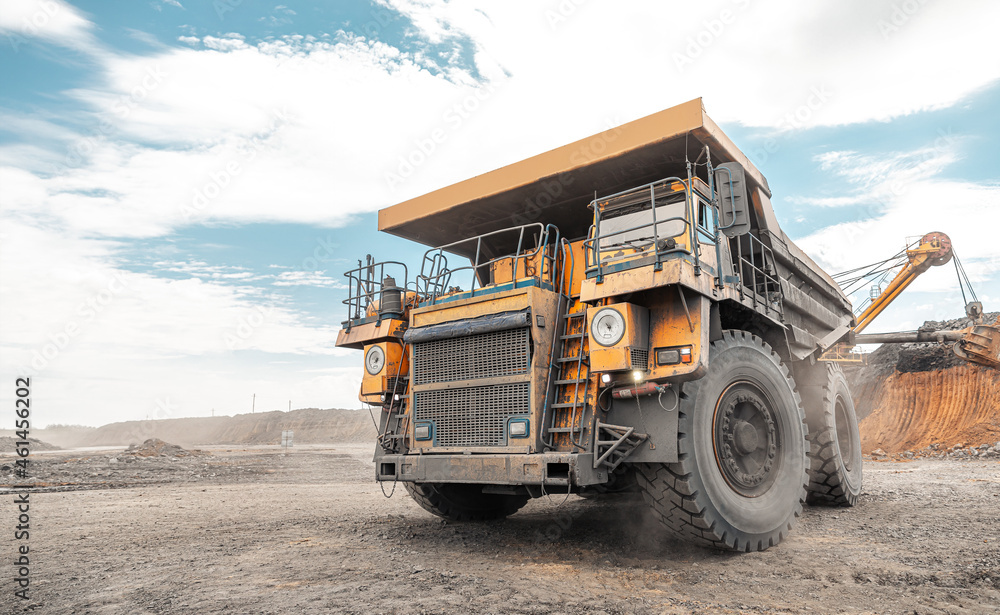 Large quarry dump truck. Big yellow mining truck at work site. Loading coal into body truck. Production useful minerals. Mining truck mining machinery to transport coal from open-pit production