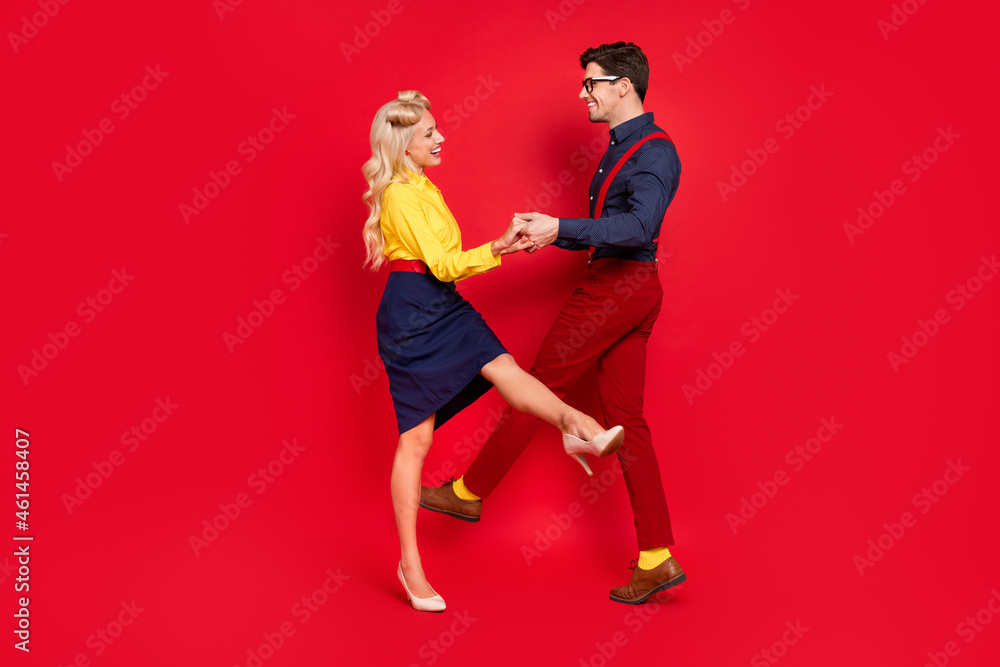 Photo of carefree funny young lady guy dressed pinup outfits dancing boogie woogie holding hands arms isolated red color background Photo of carefree funny young lady guy dressed pinup outfits dancing boogie woogie holding hands arms isolated red color background