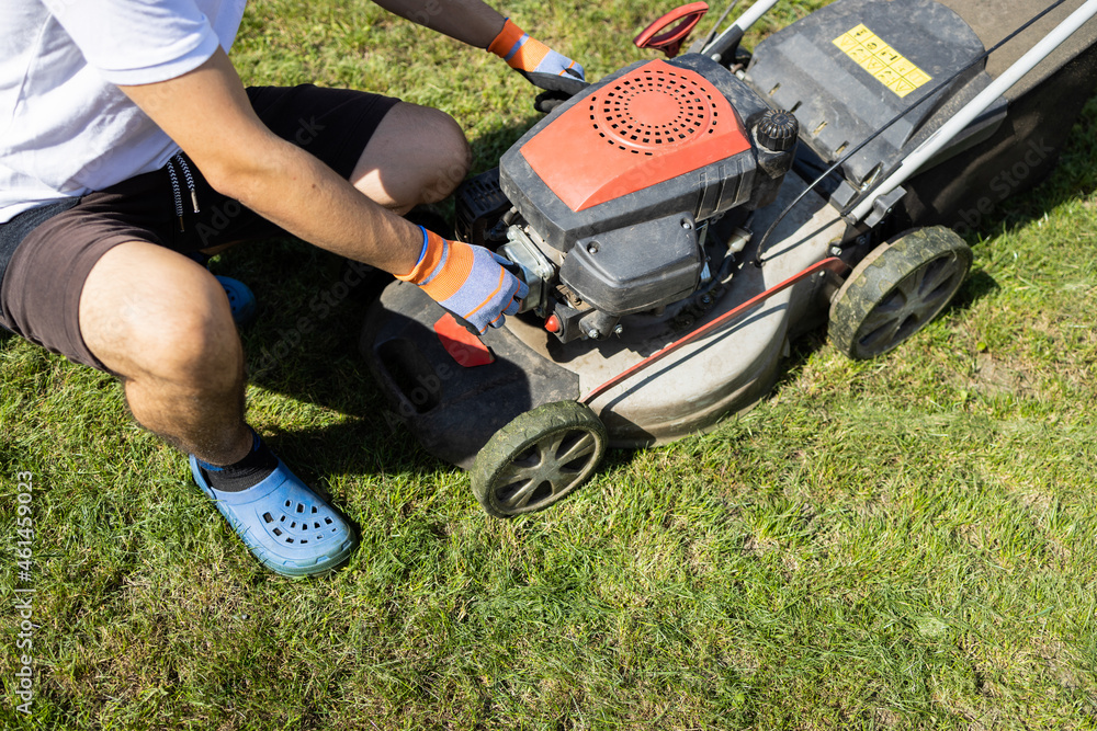 Garden worker checks a lawn mower before mowing grass in the backyard of a house Garden worker checks a lawn mower before mowing grass in the backyard of a house