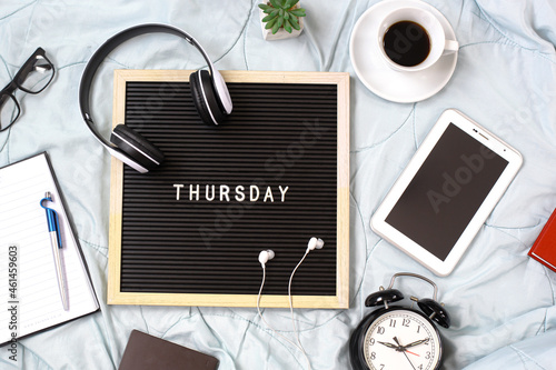 Thursday flat lay concept with multimedia accessories, books and pens, glasses, alarm clock, flowers and coffee for refreshment on white background