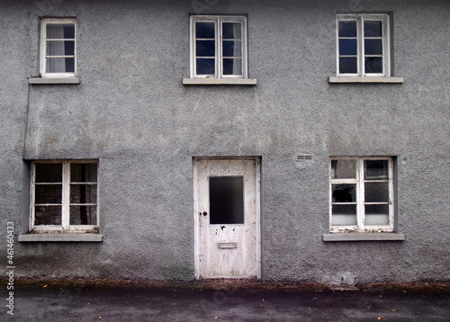 an old abandoned grey derelict house on a residential street with dirty broken windows