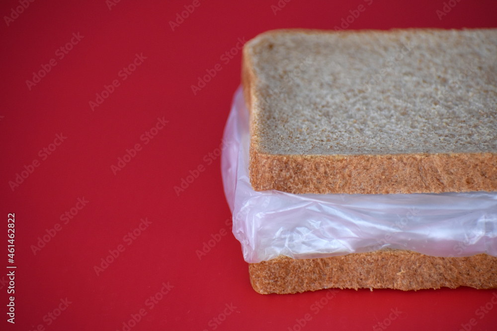 Sandwich with bread and plastic on a red background. Harmful for the food chain.
