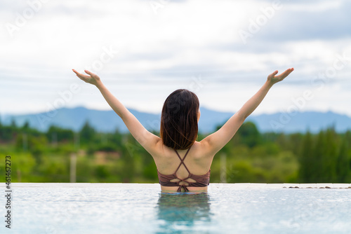 Rearview of woman in swimsuit relaxing in swimming pool at luxury hotel spa enjoying the view. © structuresxx