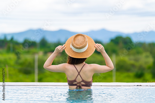Rearview of woman in sun hat relaxing at luxury hotel tropical resort swimming pool. Female enjoying summer vacation outdoors. © structuresxx