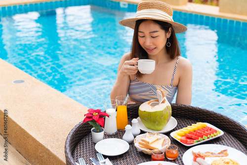 Portrait of Asian woman in swimwear enjoys floating breakfast tray in the luxury hotel resort. Female relaxing in summer vacation. © structuresxx