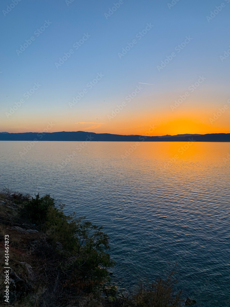 Idyllic orange sunset at the lake, silhouette of the mountains background