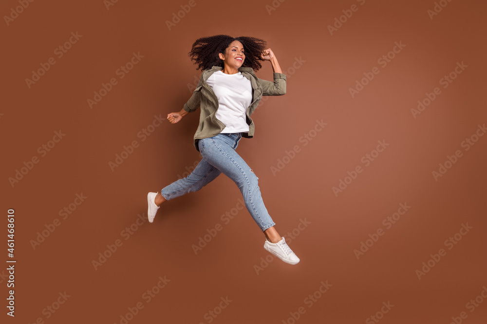Full size profile photo of funky millennial brunette lady run wear shirt jeans shoes isolated on brown background Full size profile photo of funky millennial brunette lady run wear shirt jeans shoes isolated on brown background