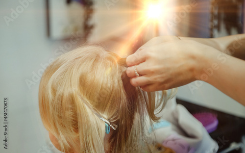 Barber woman make fashionable pretty hairstyle for cute little blond girl