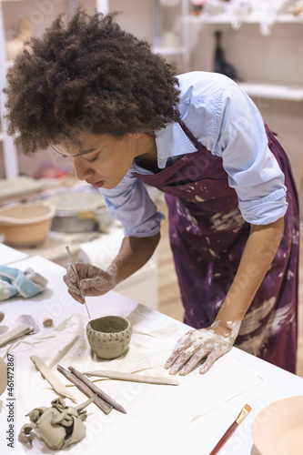 Portrait of beautiful afro american woman, pottery artist, working on clay bowl. Creative handmade craft. Ceramic studio.