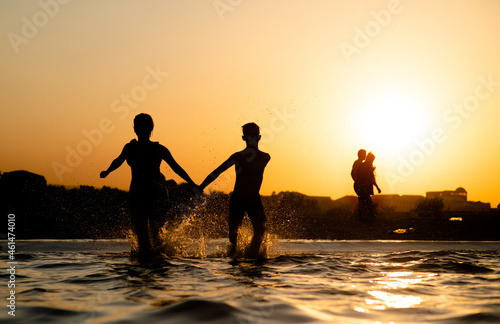 Happy friends running and splashing in the sea at sunset. Summer vacation and healthy lifestyle concept. Empty space for text
