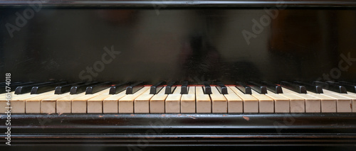 Old black grand piano keyboard with keys from ivory and ebony, part of a musical instrument in panoramic format, copy space, selected focus, narrow depth of field