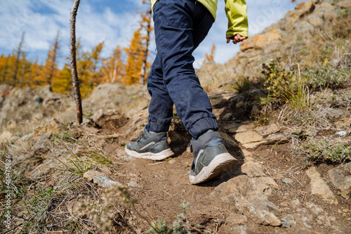 A close shot of the feet of a person climbing a mountain on a sunny autumn day, a walk in the mountains, active recreation, bright sportswear.