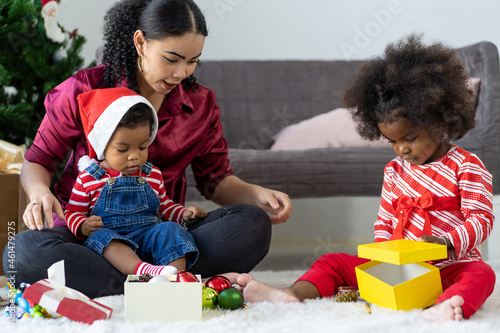 Happy family on Christmas holiday. African American mother and little girl and little son playing with decoration items for Christmas tree at home. Merry Christmas and Happy Holidays