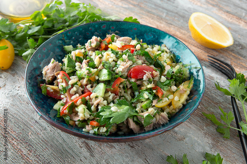 bowl of Lebanese tabbouleh salad with vegetables, bulgur and canned tuna on a wooden table photo
