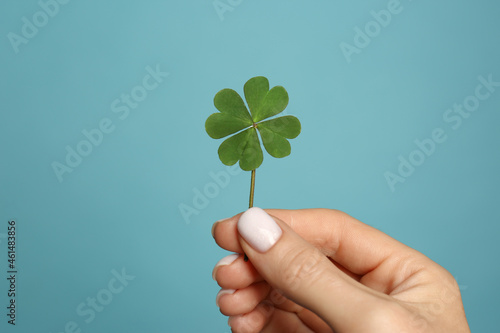 Woman holding green four leaf clover on light blue background, closeup photo