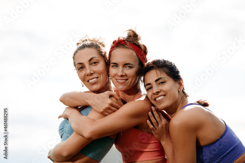 Group of three woman warms up in park before jogging. Healthy lifestyle concept. Sporty females friends having fun and doing different stretching exercises in summer park.