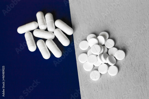 two forms of medicinal tablets; a handful of oval long pills and a bunch of round pressed pills on a modern designer background of two different colors - gray and dark violet