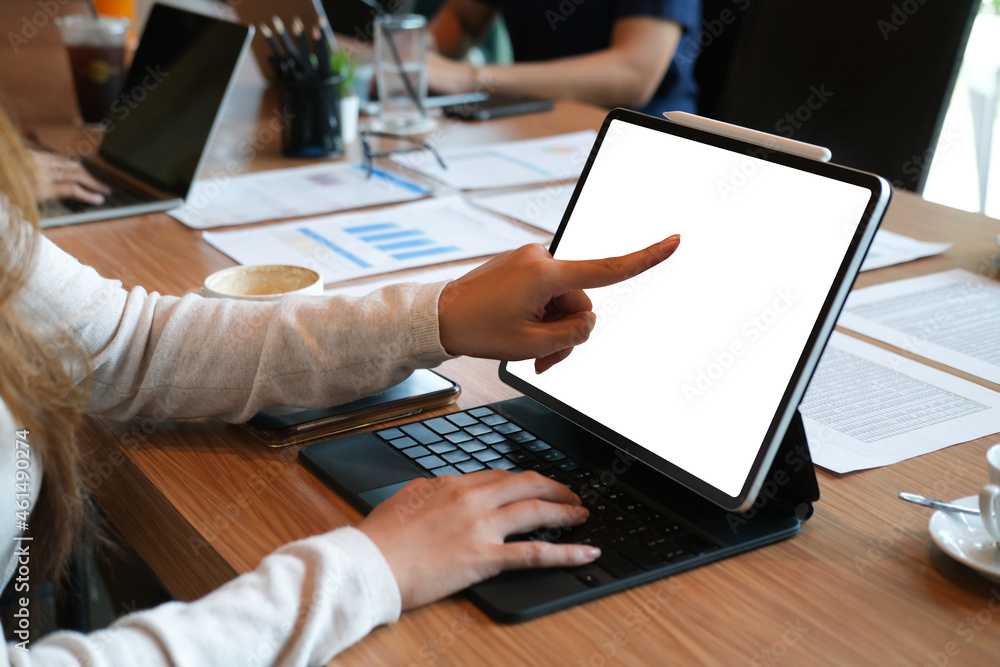 Cropped image of young female pointing finger to a white screen digital tablet at the wooden table while making a business meeting. Cropped image of young female pointing finger to a white screen digital tablet at the wooden table while making a business meeting.