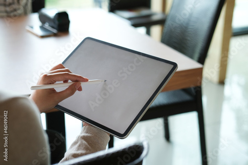 Cropped image of a woman's hands is using a stylus pen and a white screen digital tablet over the wooden working desk as a background.
