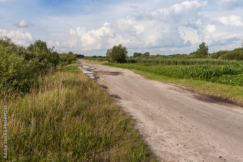 Broken country road with puddles among the fields