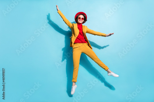 Photo of shiny sweet young woman dressed red headwear jumping high smiling isolated blue color background