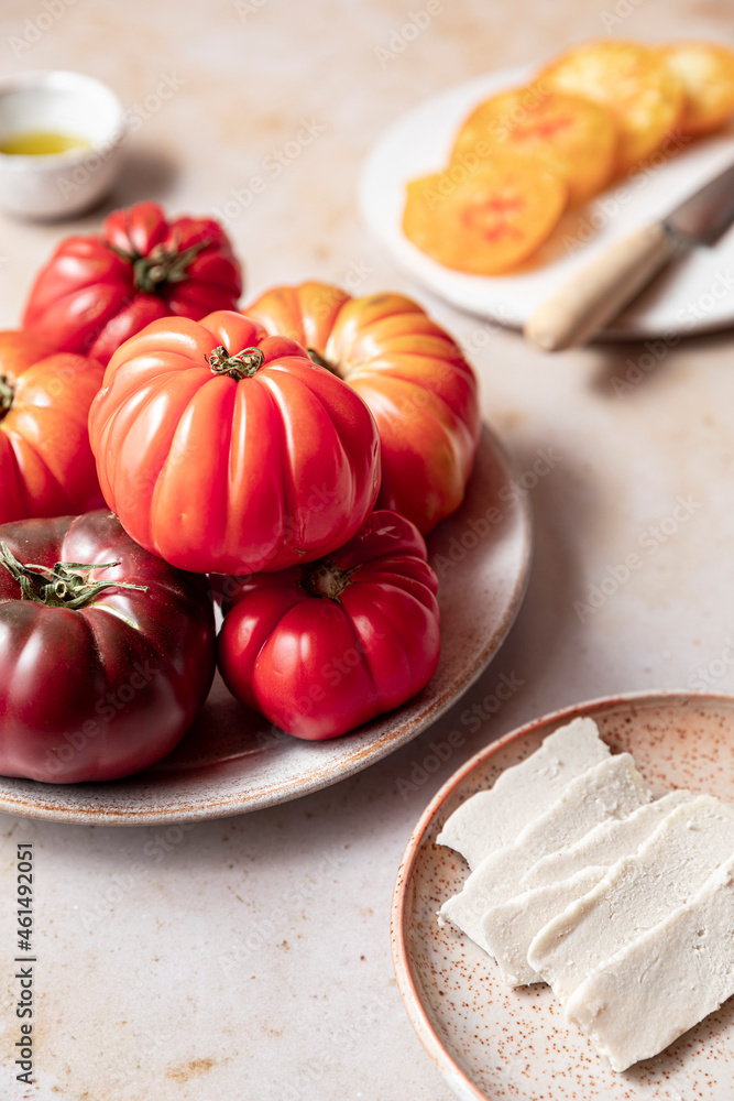 A plateful of heirloom tomatoes and vegan mozzarella chese shot on a beige marble surface A plateful of heirloom tomatoes and vegan mozzarella chese shot on a beige marble surface