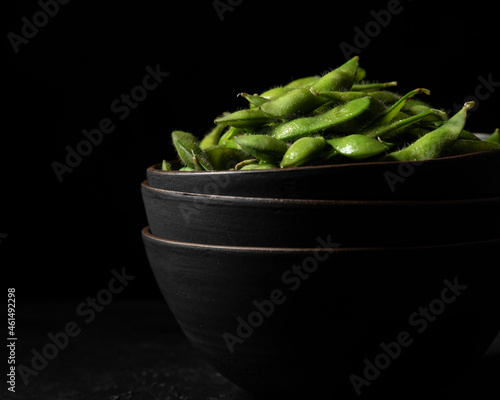 Black ceramic bowls filled with bright green edamame pods shot against a black background photo