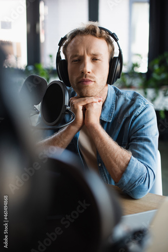 focused radio host in wireless headphones near microphone in studio