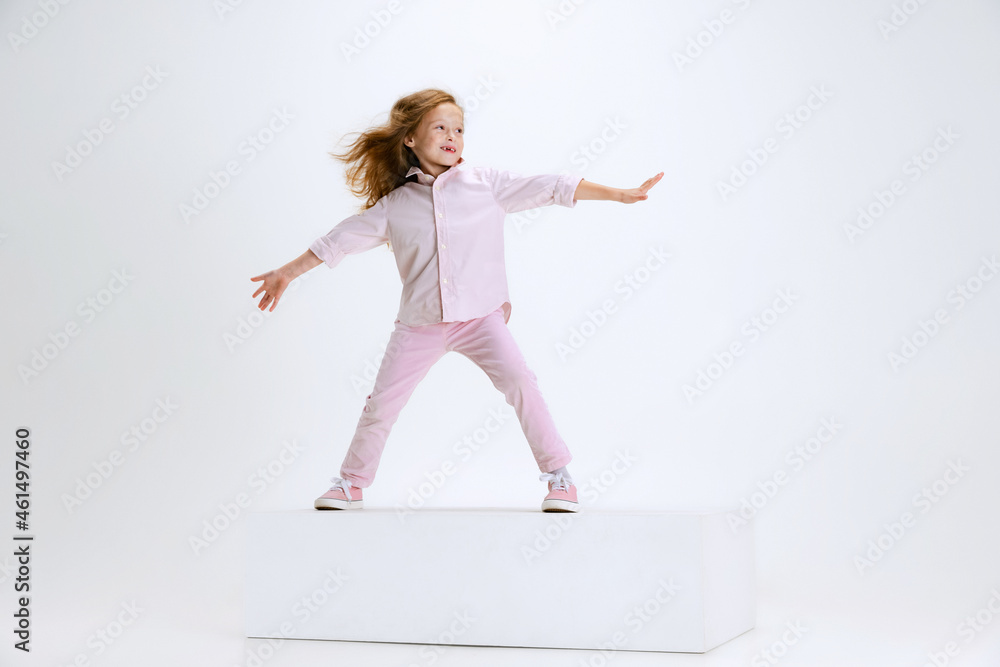 Full-length portrait of smiling girl in casual clothes standing on big box isolated on white studio background. Happy childhood concept.