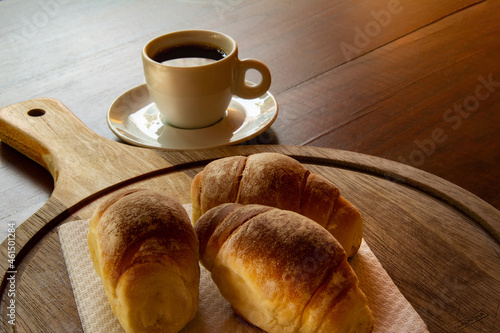 Três pães caseiros sobre uma tábua e uma xícara de café preto. Café da manhã.