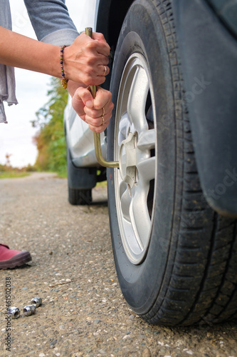 woman changing wheel, hands unscrewing bolts on flat car tire on the road.