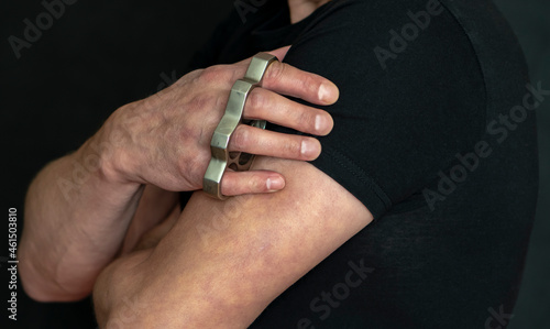 A man holds a brass knuckles in his hand on a dark background, close-up, selective focus. Concept: attack by robbers, street gangs, self-defense against hooligans.