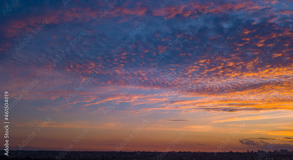 End of the day with a sky between clouds and very colorful, highlighting blue and orange. At the base of the image, and in the background, is the silhouette of the city.
