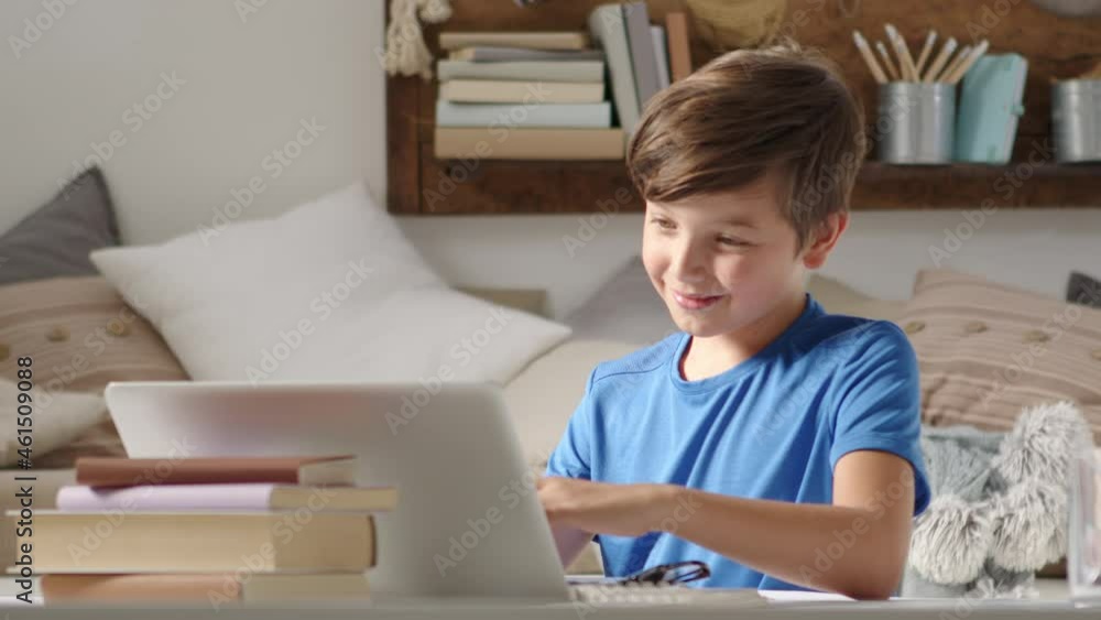 smiling student boy studying at home with remote school connected to computer on the web, raise his hand to answer questions or greet his classmates, sitting at desk full of books smiling student boy studying at home with remote school connected to computer on the web, raise his hand to answer questions or greet his classmates, sitting at desk full of books