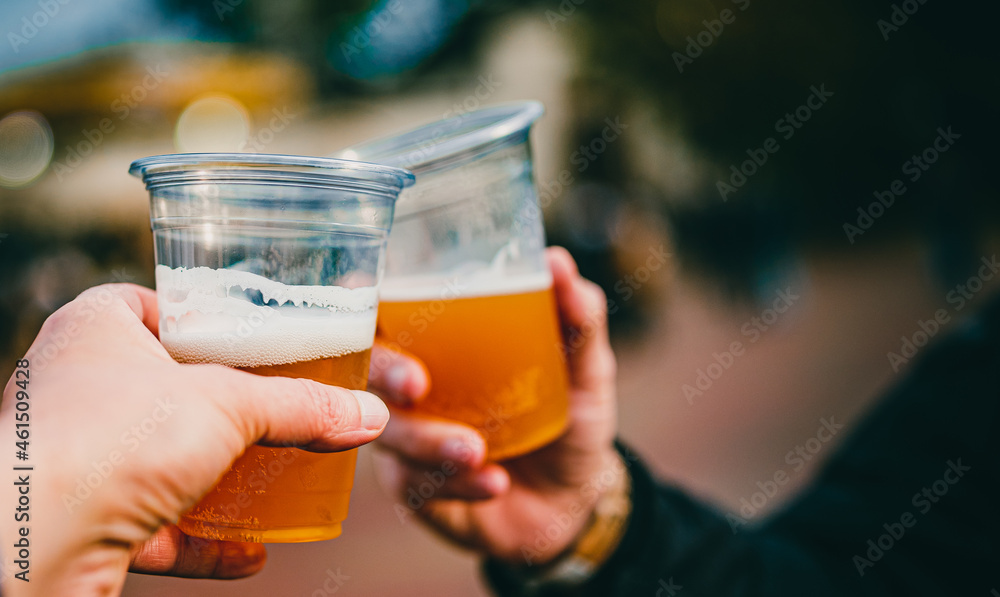 two plastick glass of beer in hand. Beer clinking outdoor - obrazy, fototapety, plakaty 