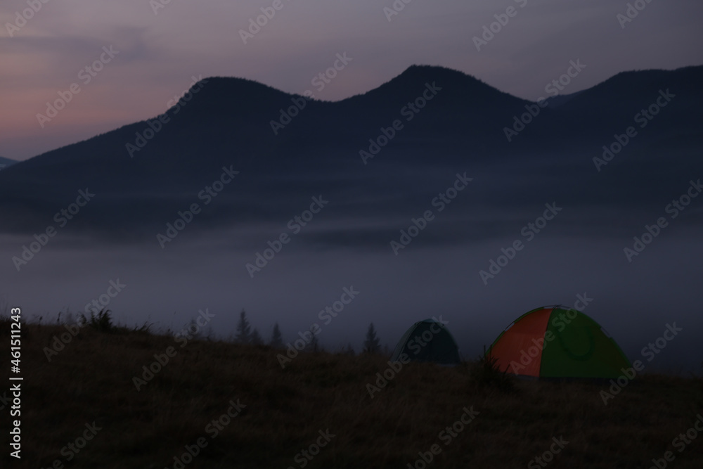 Picturesque view of mountain landscape with thick fog and camping tents at dawn
