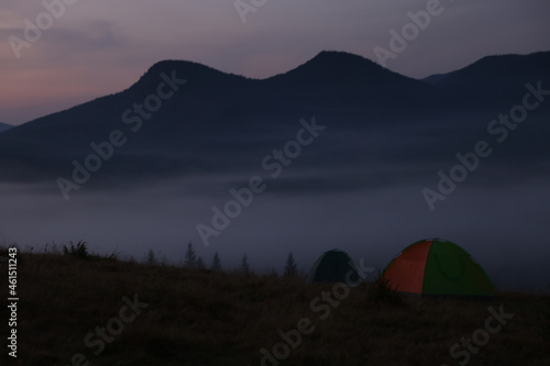 Picturesque view of mountain landscape with thick fog and camping tents at dawn