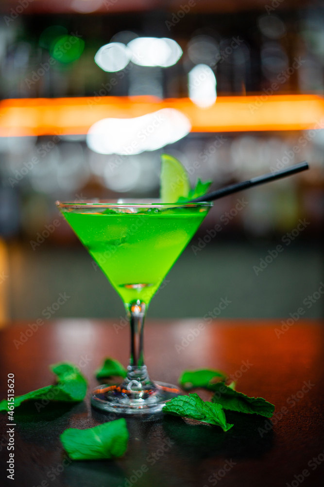Glass of green cocktail on bar counter with mint and lemon. Selective focus Glass of green cocktail on bar counter with mint and lemon. Selective focus