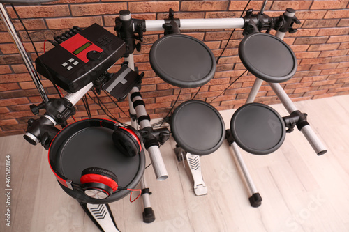 Modern electronic drum kit with headphones near red brick wall indoors, above view. Musical instrument
