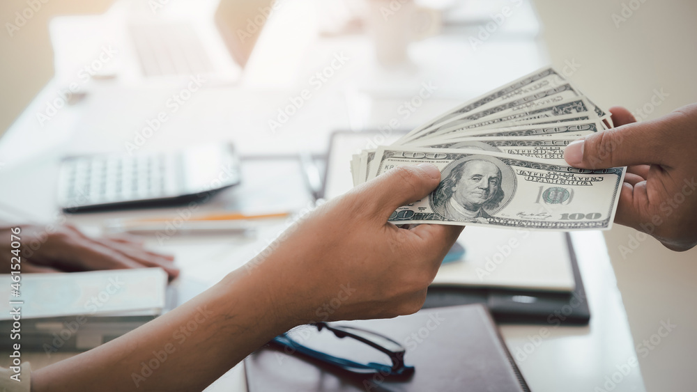 Fototapeta premium Man offering batch of hundred dollar bills. Hand of a businessman giving money to his partner. Hand receiving money from businessman. Venality, bribe, corruption concept.