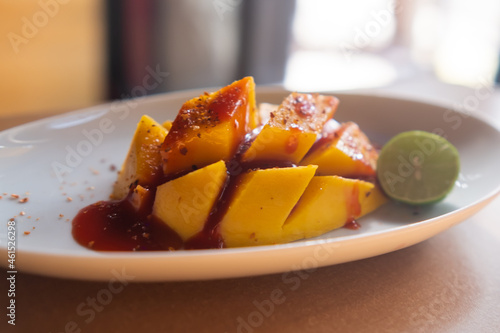 Plate of chopped mango with Mexican chamoy sauce and blurry background