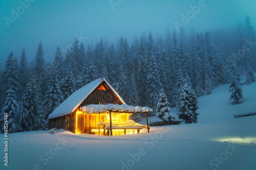 Fotografia, Obraz Fantastic winter landscape with glowing wooden cabin in snowy forest