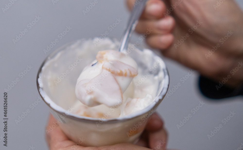 Hands holding spoon and cup of peaches and cream with light blue background Hands holding spoon and cup of peaches and cream with light blue background