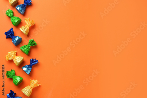Many candies in colorful wrappers on orange background, flat lay. Space for text