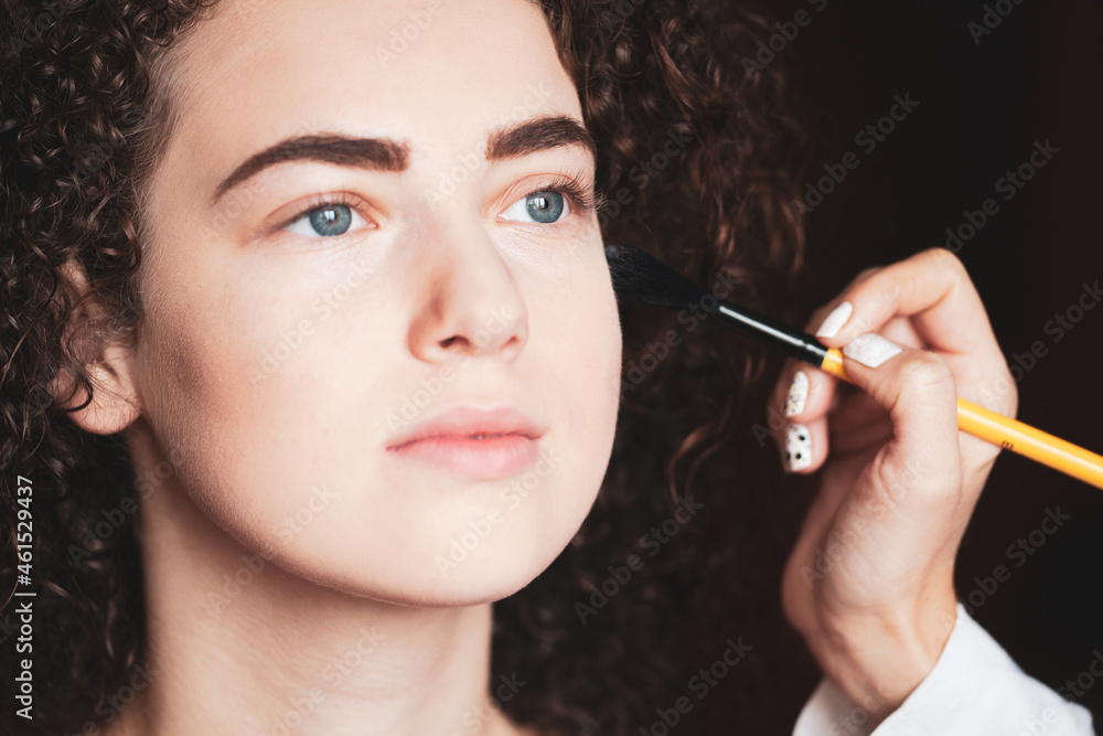 The work of a professional makeup artist. Closeup portrait of beautiful woman getting professional make-up with brush.