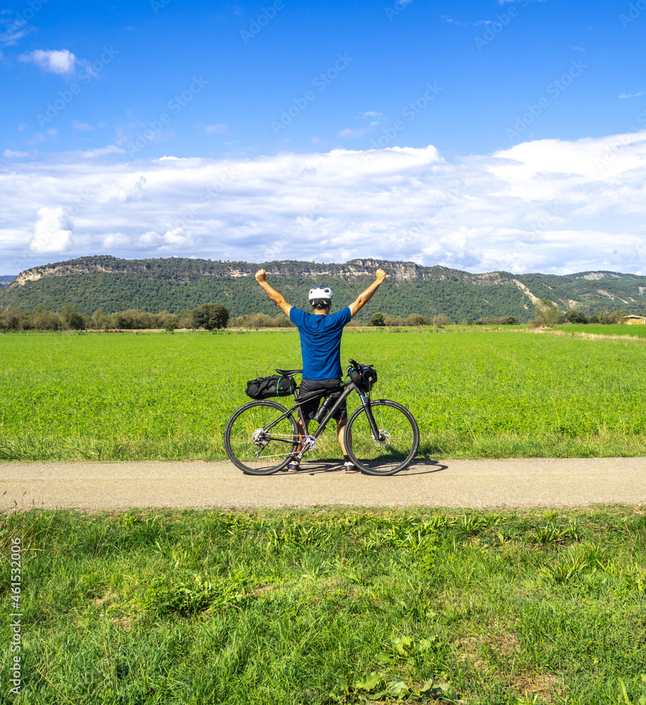 Obraz premium Adventurous cyclist man traveling in nature raises his hands as a symbol of victory. Bikepacking