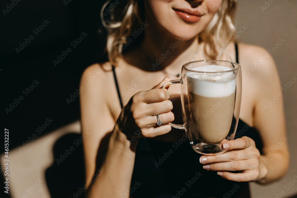 Closeup of a woman holding a transparent cup of coffee with latte in sunlight, smiling. Closeup of a woman holding a transparent cup of coffee with latte in sunlight, smiling.