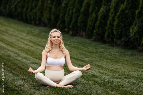 Pregnant woman wearing sportswear, meditating, sitting in yoga pose.