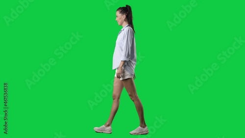 Side view of happy relaxed summer style smart casual woman walking. Full body on green screen chroma key background